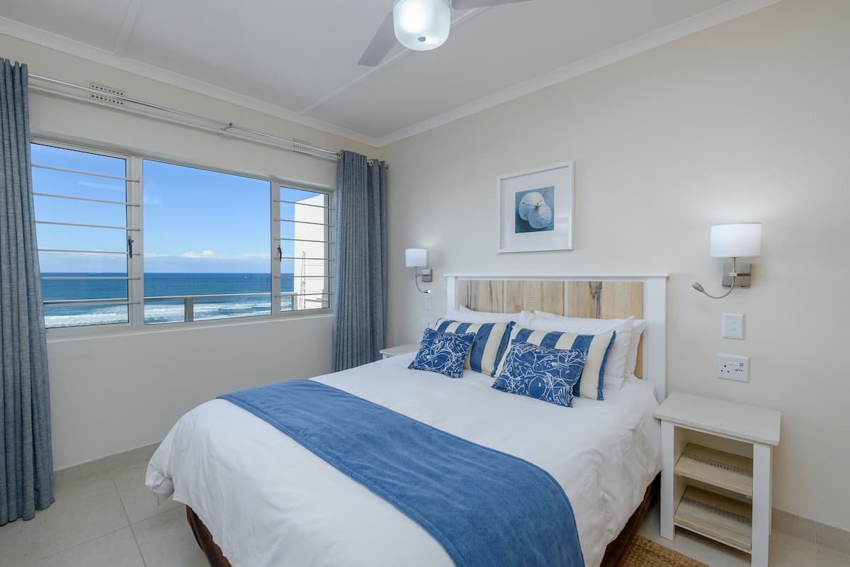 A bedroom with a large bed, a view of the ocean, and a ceiling fan.