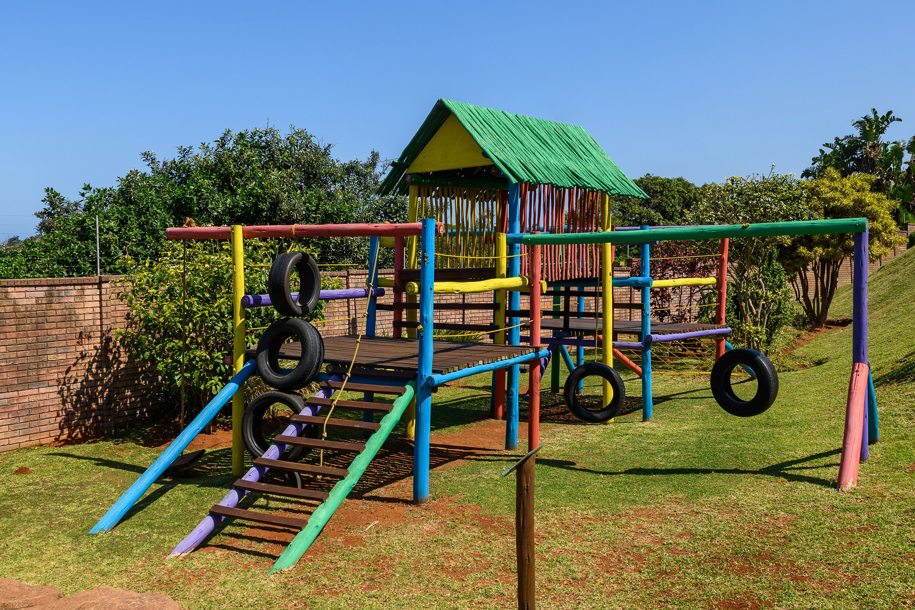 A playground with a green-roofed playhouse, tire climbing wall, and colorful play structures.