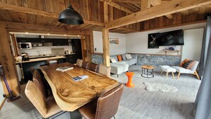 Un interior rústico con una mesa de comedor de madera, sillas de cuero, una pared de acento de piedra y una zona de estar acogedora con sofá y reposapiés.