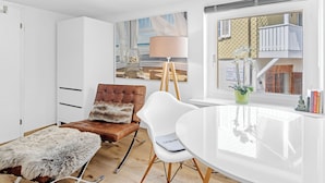 A modern living room with a white sofa, a brown leather armchair, a white dining table, and a large window with a view of a building. - HouseofHarmony (Stafa)