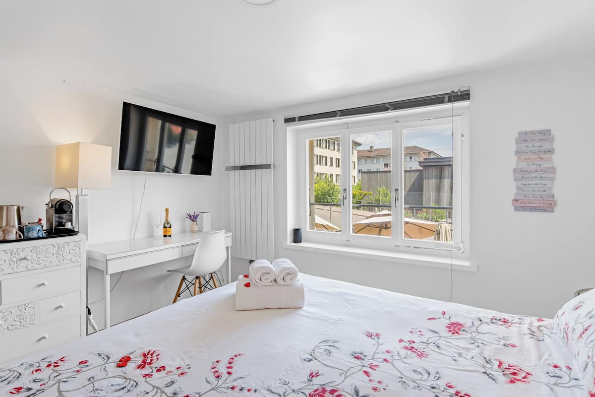 A hotel room with a bed, a desk, a chair, a TV, and a window with a view of buildings.