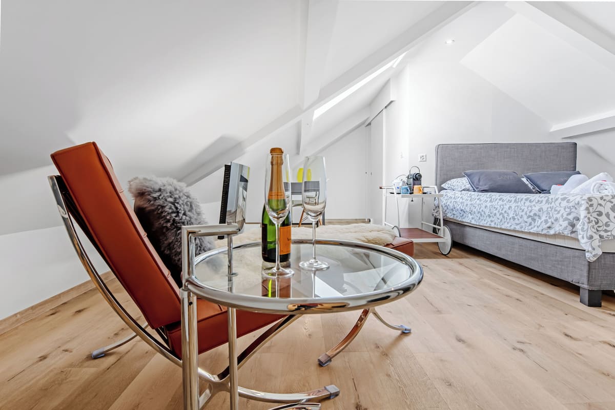 A modern loft bedroom with a glass table, a red chair, and a bed with patterned bedding.