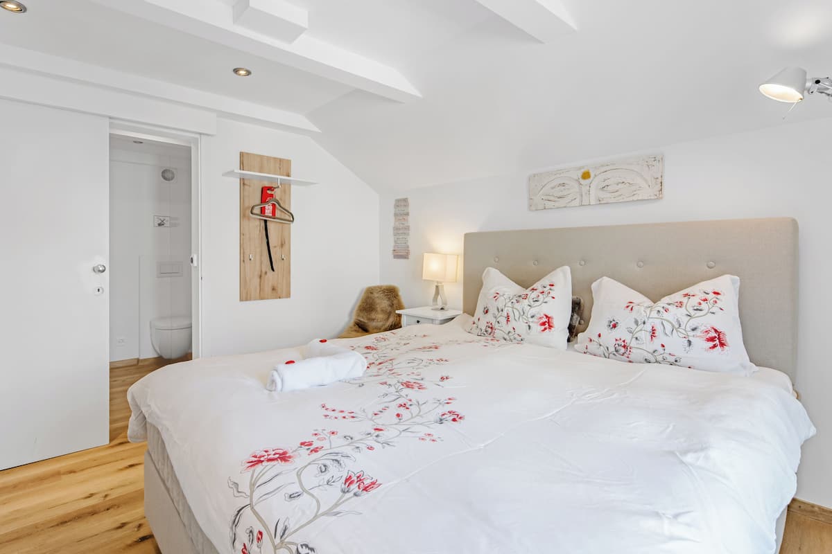 A bedroom with a large bed, a wooden headboard, a nightstand, a lamp, and a wall-mounted shelf with a fire extinguisher.