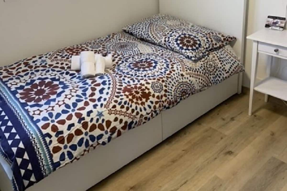 A small, neatly arranged bedroom with a bed, a bedside table, and a window.