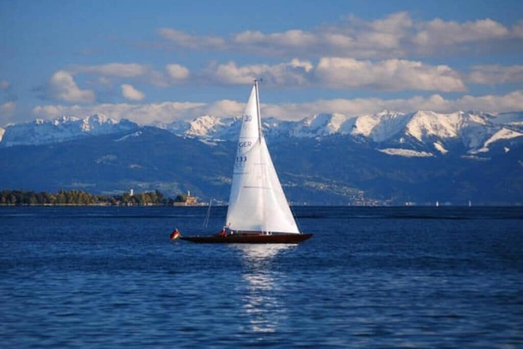 Un velero en un lago tranquilo con montañas nevadas al fondo.