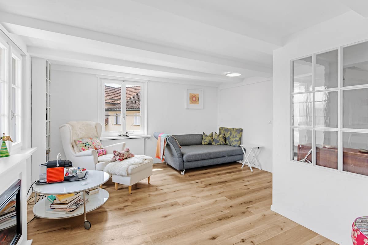 A modern living room with a white fireplace, a grey sofa, a white armchair, and a coffee table.