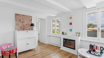 Un salon moderne avec une cheminée, un plancher en bois, un fauteuil à motifs floraux rouges et une vue sur les immeubles à travers de grandes fenêtres.