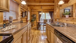 A wooden cabin interior with a kitchen featuring wooden cabinets, a granite countertop, a dining table with chairs, and pendant lighting.
