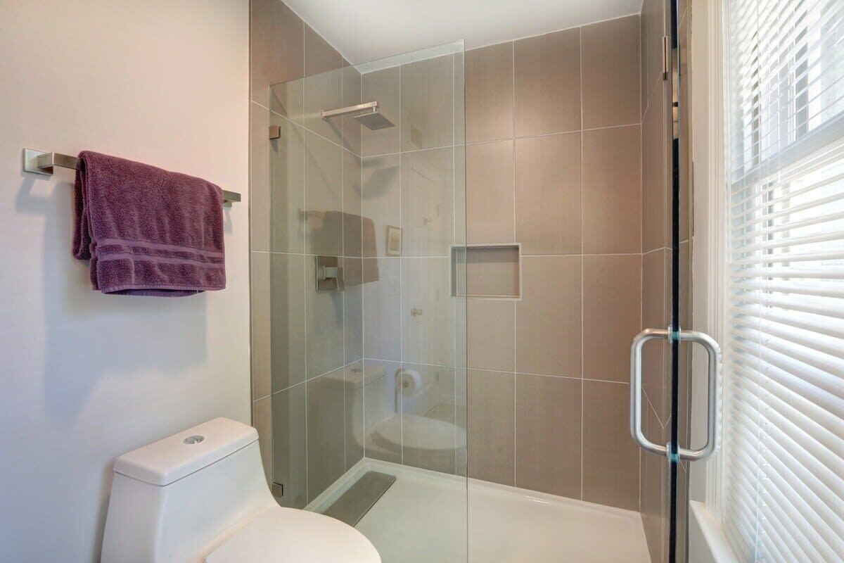 A bathroom with a glass shower enclosure, a toilet, and a towel rack.