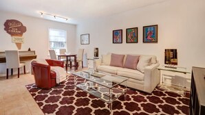 A modern living room with a white sofa, red chair, glass coffee table, and artwork on the wall.
