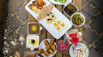 A variety of food items and drinks arranged on a wooden table outdoors.