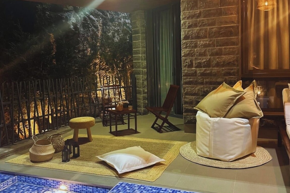 A cozy outdoor seating area with a pool, stone walls, and a hanging light fixture.
