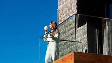 A person on an outdoor balcony with a modern architectural design, featuring wooden panels and glass railings.