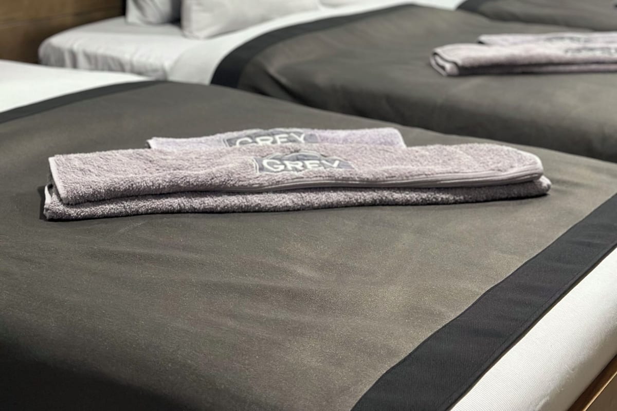 Ein Hotelzimmer mit zwei Betten, grauer Bettwäsche und einem Holzkopfstück.