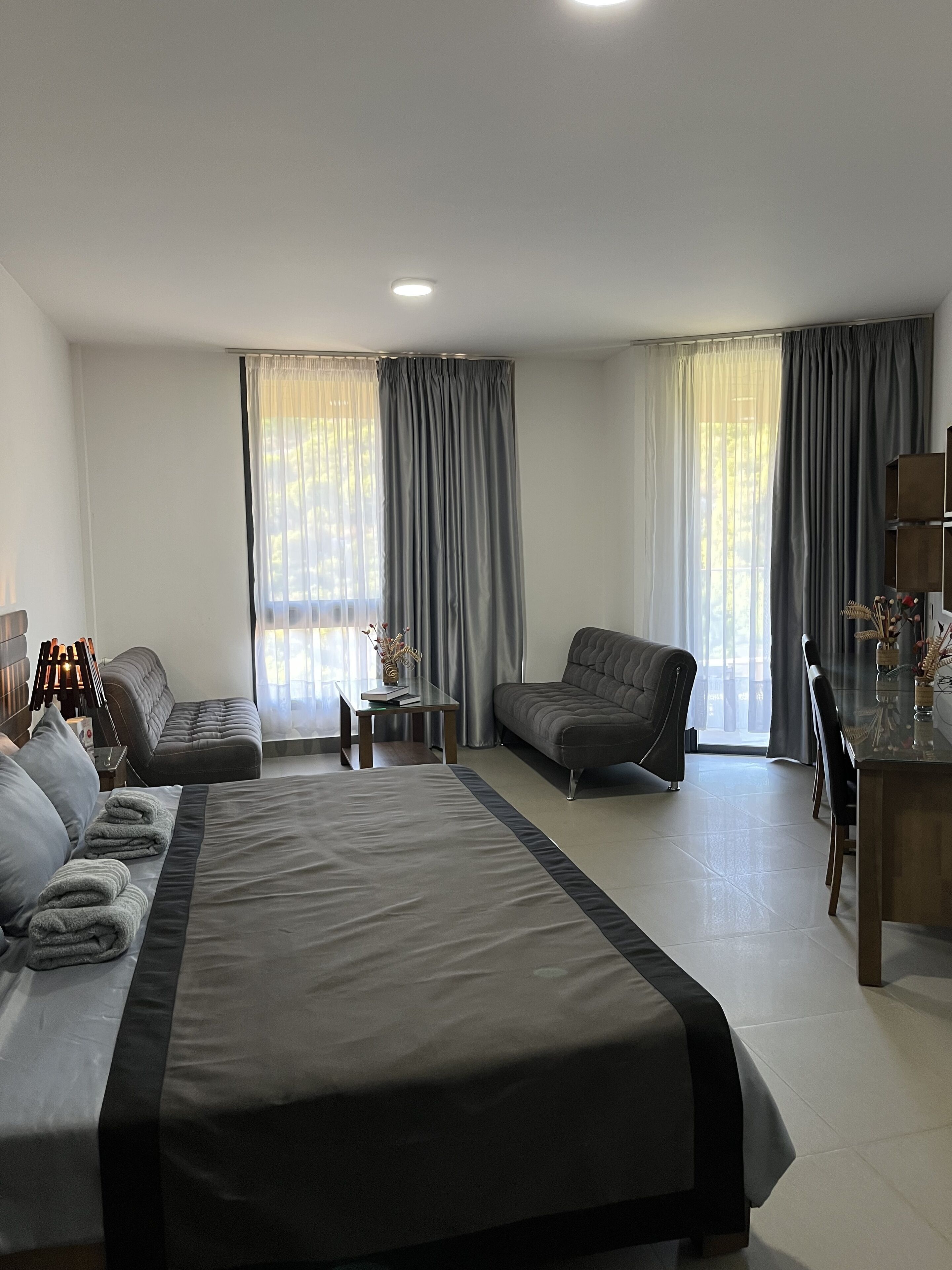A modern hotel room with a large bed, a sofa, a small table, and a dining area.