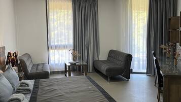 A modern hotel room with a large bed, a sofa, a small table, and a dining area.
