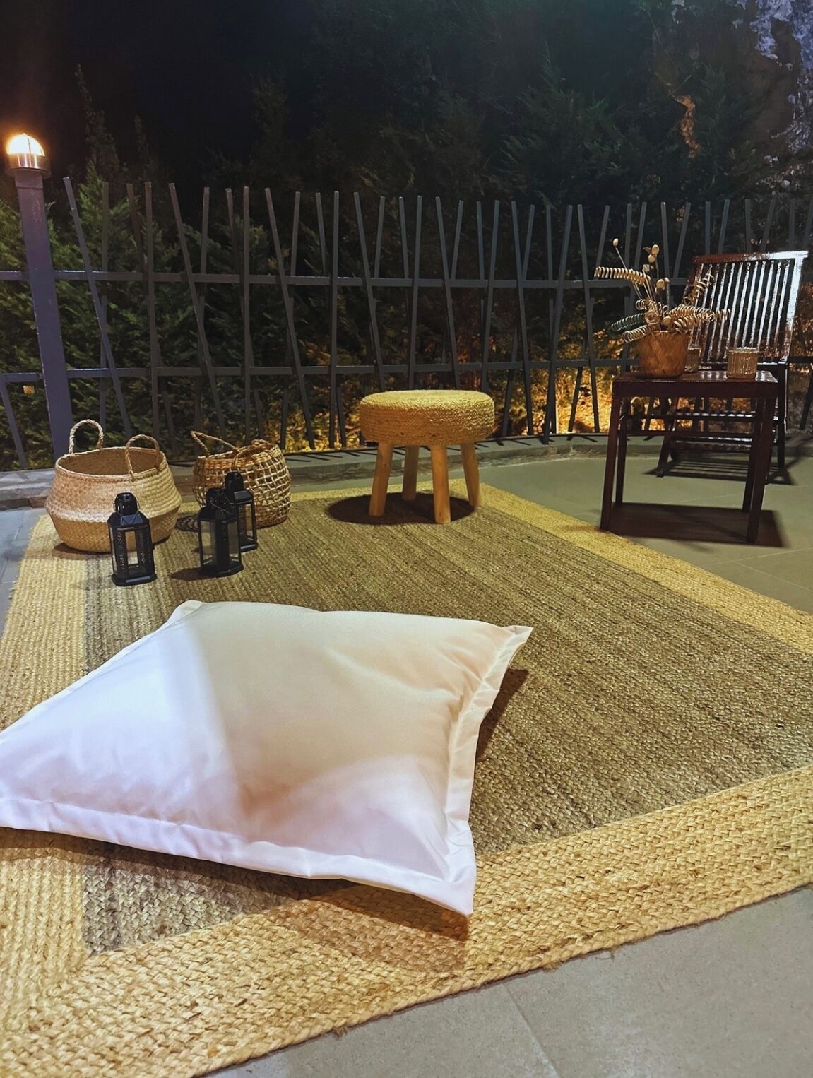 An outdoor seating area with a woven mat, a white cushion, wicker baskets, and a wooden stool.