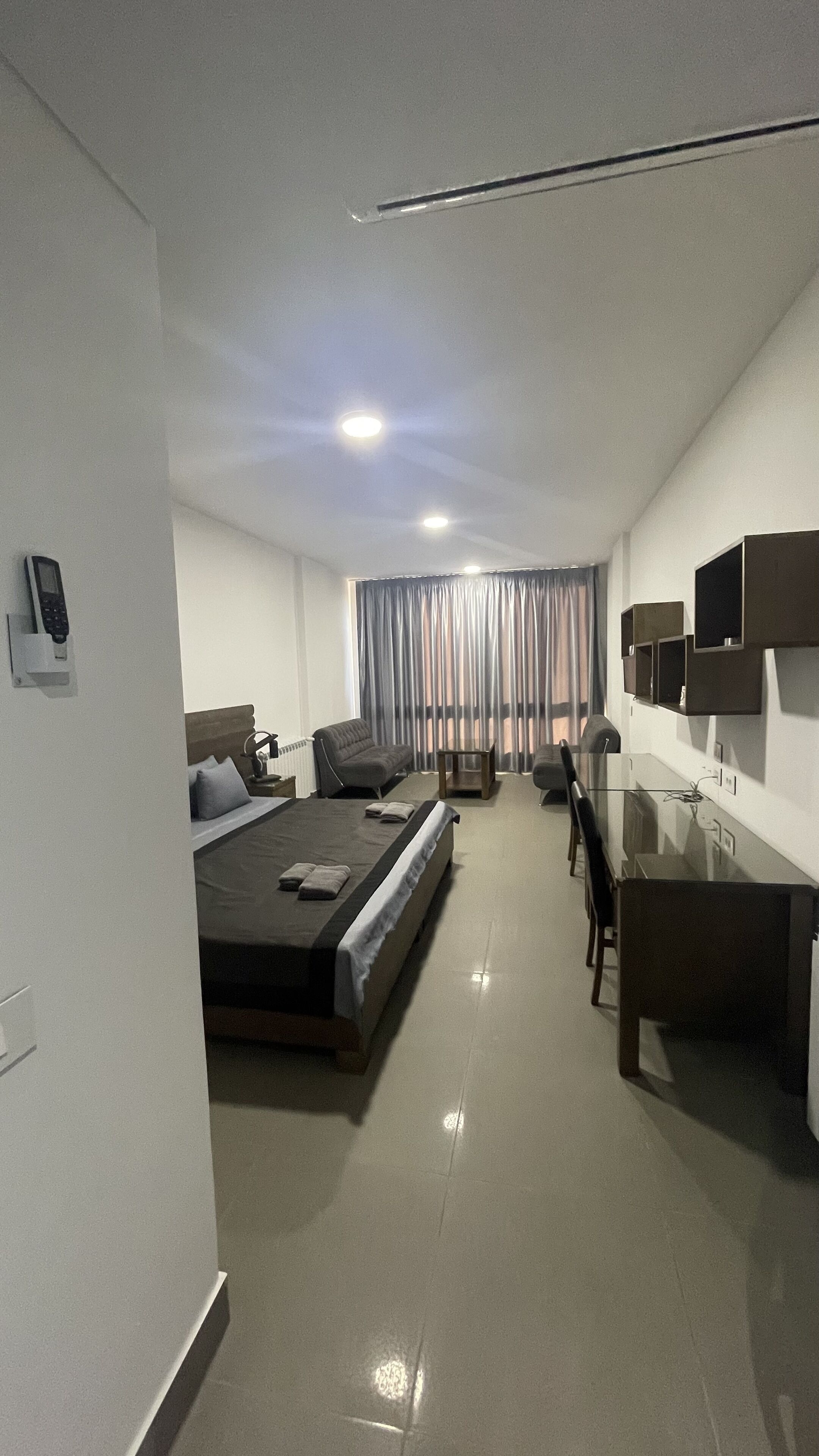 Una habitación de hotel moderna con cama, escritorio, silla y televisor en la pared.