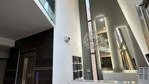 Een moderne receptiebalie met een glazen scheidingswand, een digitaal displayscherm voor de lift en een decoratieve metalen sculptuur.
