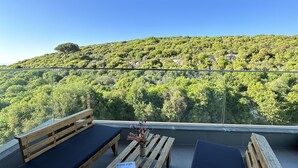 Een houten terras met twee banken en een tafel, met uitzicht op een groene heuvel.