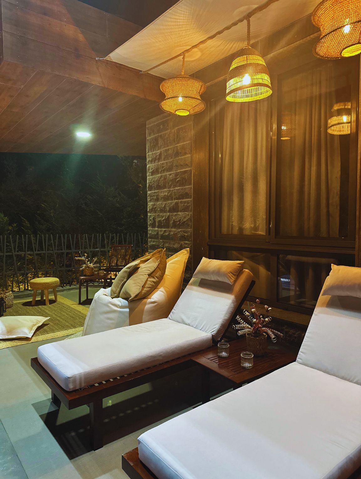 A lounge area with two reclining chairs, a stone wall, and a window with curtains.