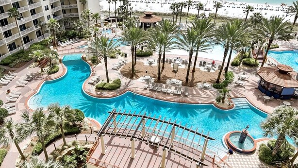 A resort pool area with a large central pool, surrounded by palm trees and lounge chairs. - Family Perfect with Lagoon pool and Crystal Sand Beach! (Panama City Beach)