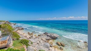 Vista costera con un litoral rocoso, mar azul cristalino y una terraza de madera con vista al océano.