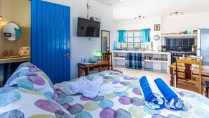Una habitación con cama, escritorio, televisión y kitchenette.