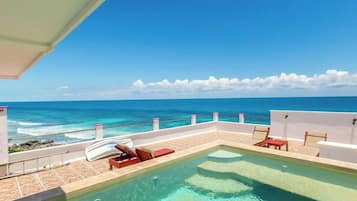 Una piscina sul tetto con acqua cristallina, pareti bianche e poltrone da relax rosse.