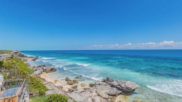 A coastal view with a rocky shoreline, clear blue sea, and a wooden deck overlooking the ocean.