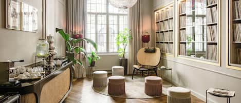 Una habitación con piso de madera, un candelabro, una estantería y una mesa con lámpara.