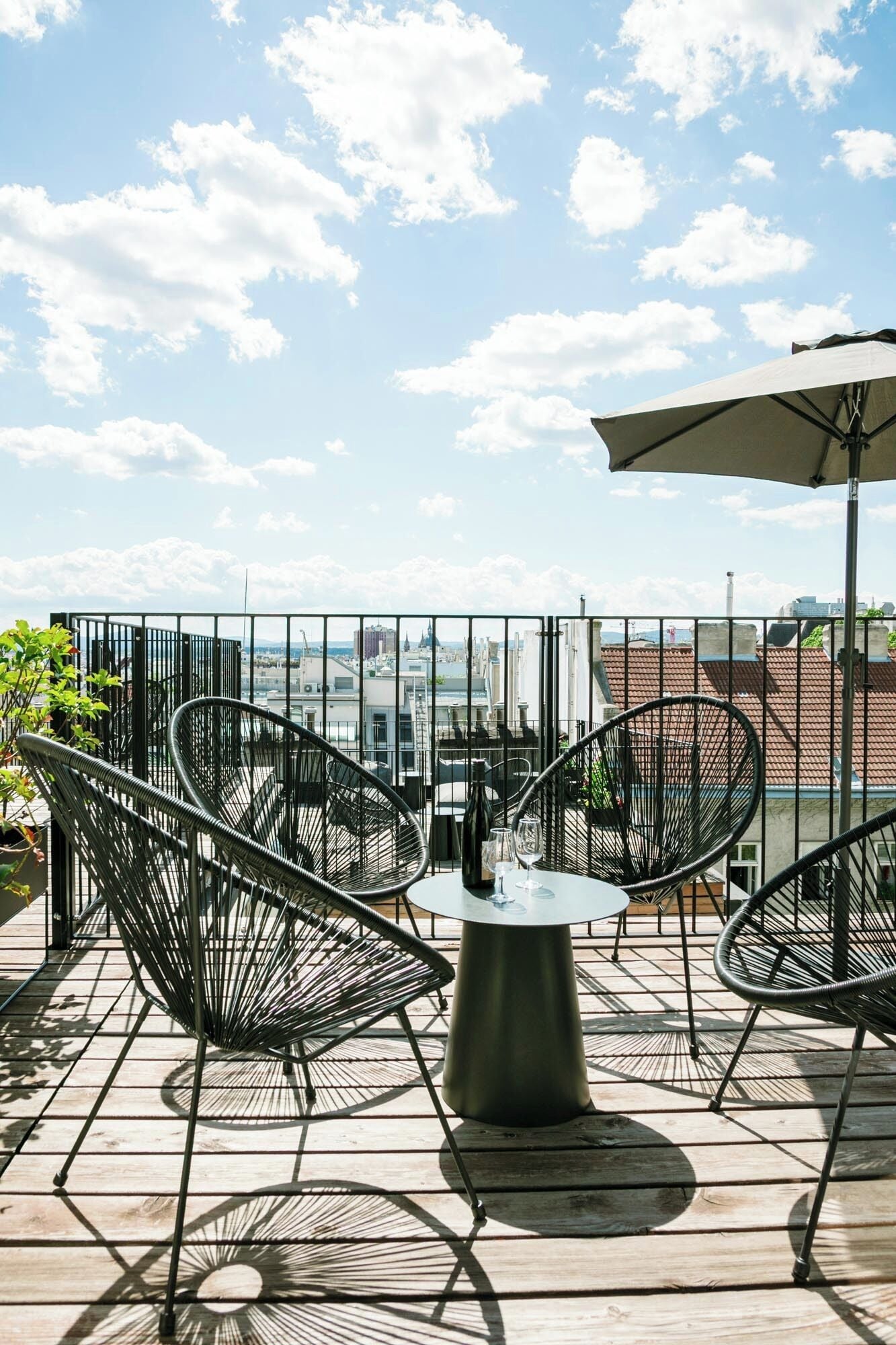 Een terras op het dak met een tafel en stoelen, een uitzicht over de stad en een metalen hek.