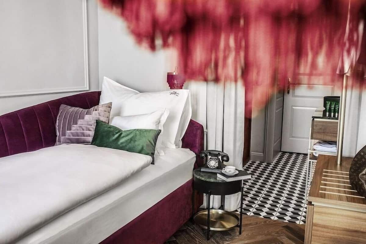 A modern bedroom with a red sofa, white bedding, a small side table with a telephone, and a checkered floor.