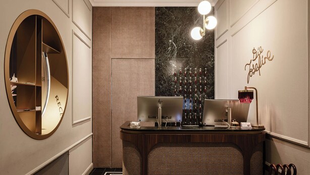 Zona de recepción de un hotel, con mostrador de recepción, enfriador de vino integrado en la pared y un letrero decorativo.