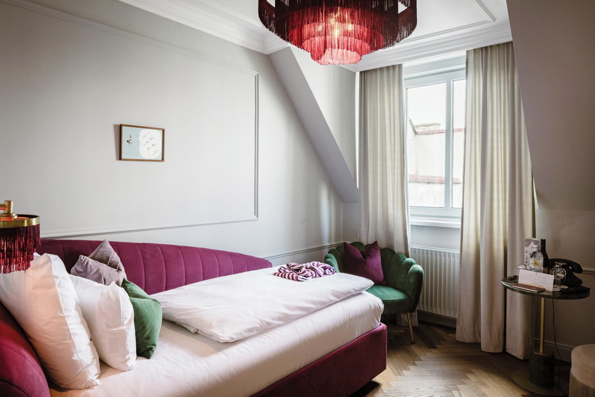 Ein modernes Schlafzimmer mit einem Bett, einem grünen Sessel, einem roten Sofa und einer Deckenleuchte.