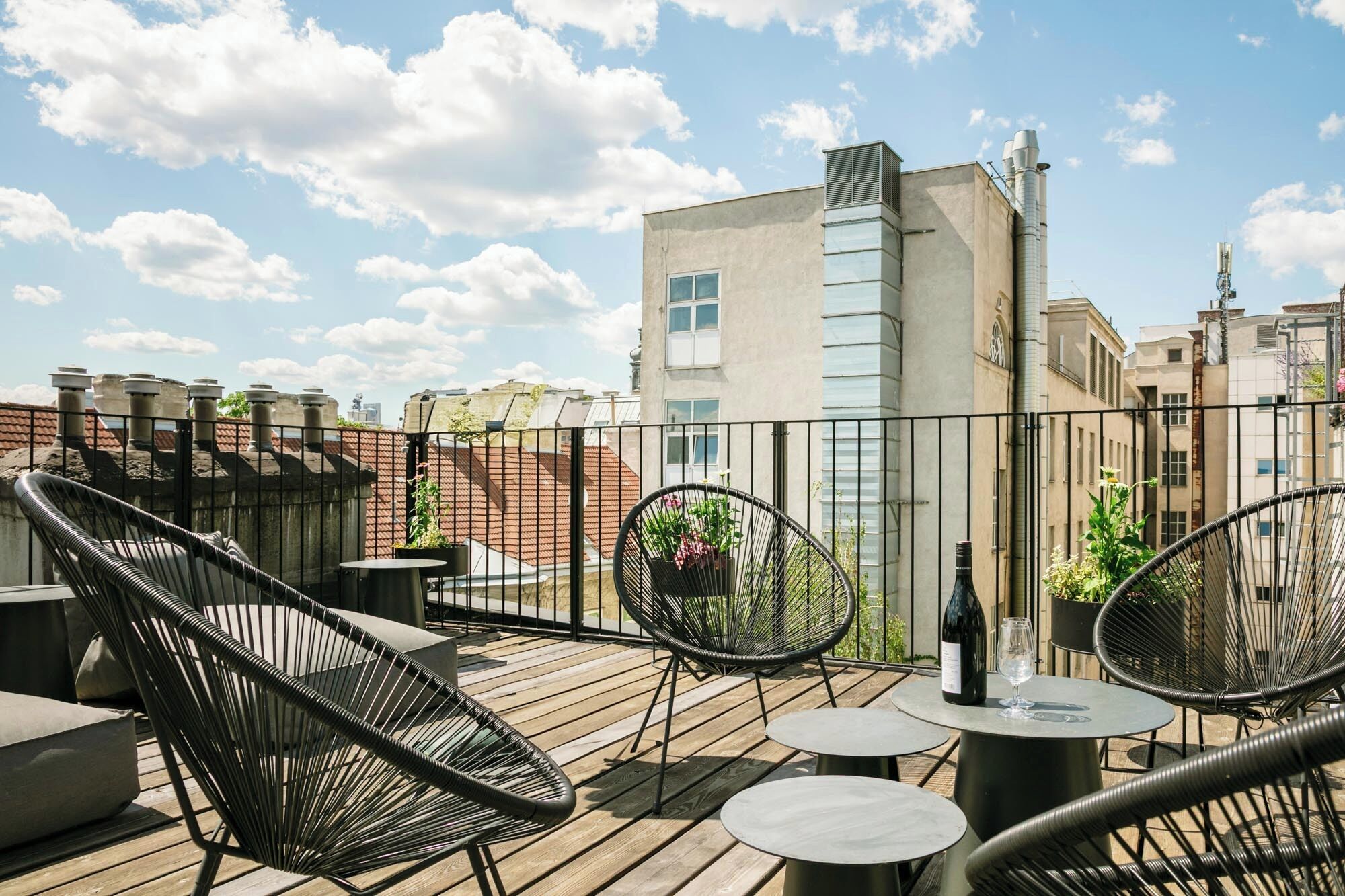 A rooftop terrace with outdoor seating, including chairs and tables, and a view of the cityscape in the background.