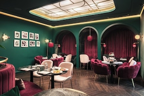 A dining area with round tables, cushioned chairs, and a green wall with framed pictures. - Eurostars Josefine (Vienna)