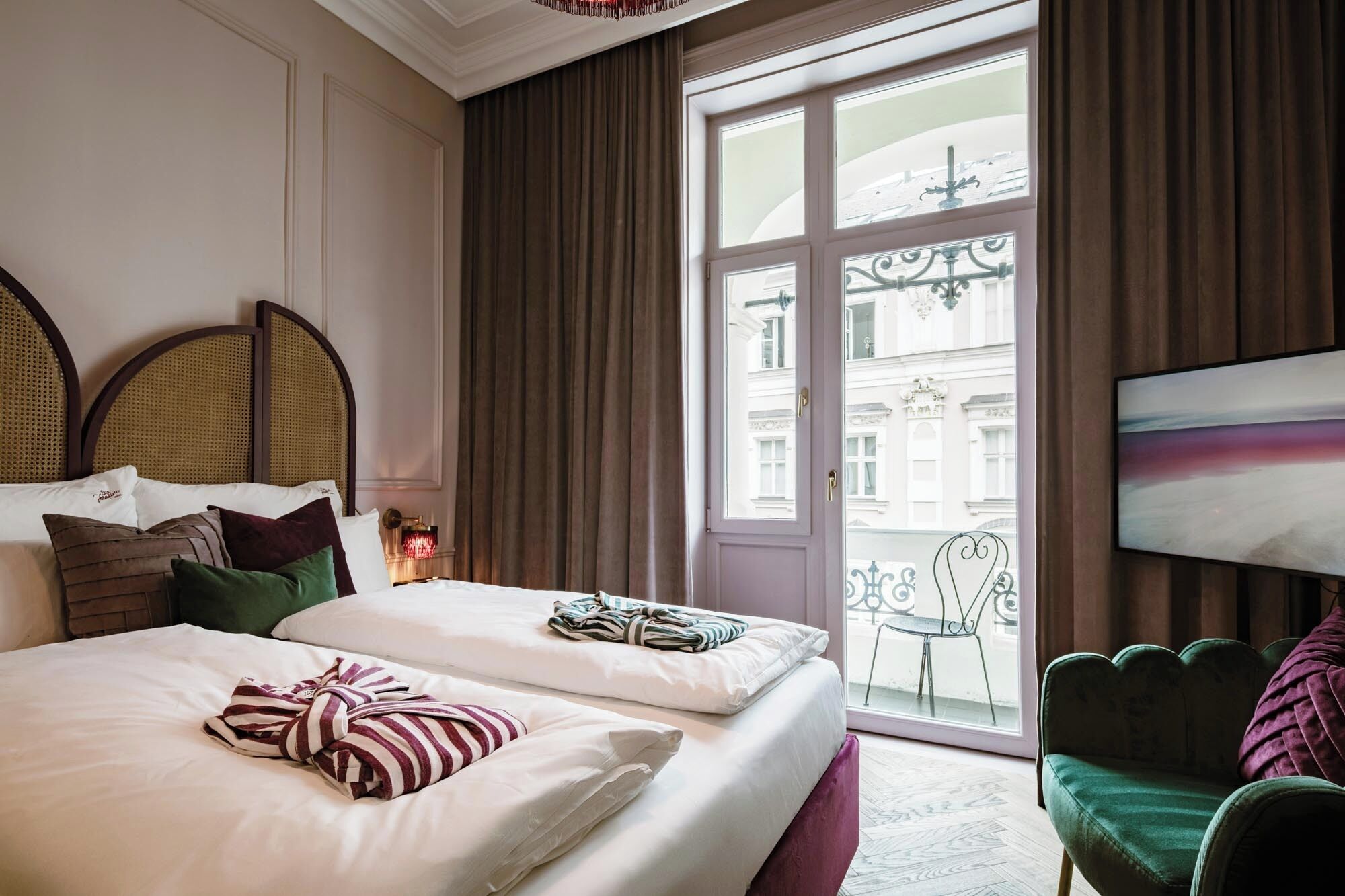 Habitación de hotel con una cama grande, un sillón verde y vista a un edificio a través de un ventanal.