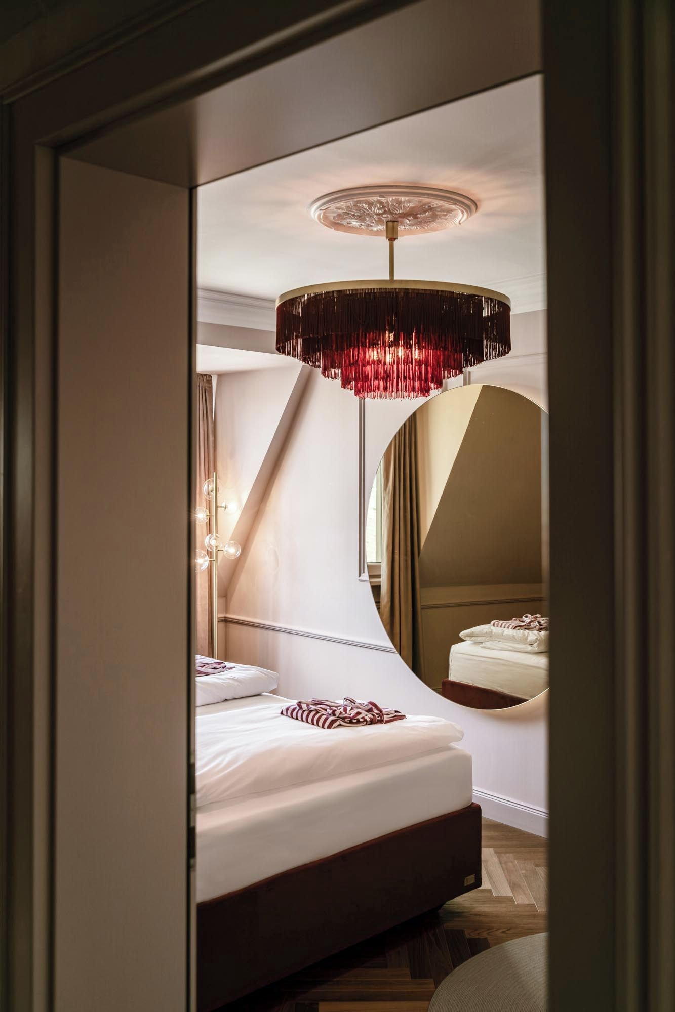 Une chambre moderne avec un grand lit, un lustre original et un miroir qui reflète la pièce.