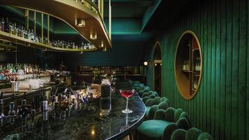 A bar area with a curved marble countertop, green upholstered seating, and a large mirror on the wall.