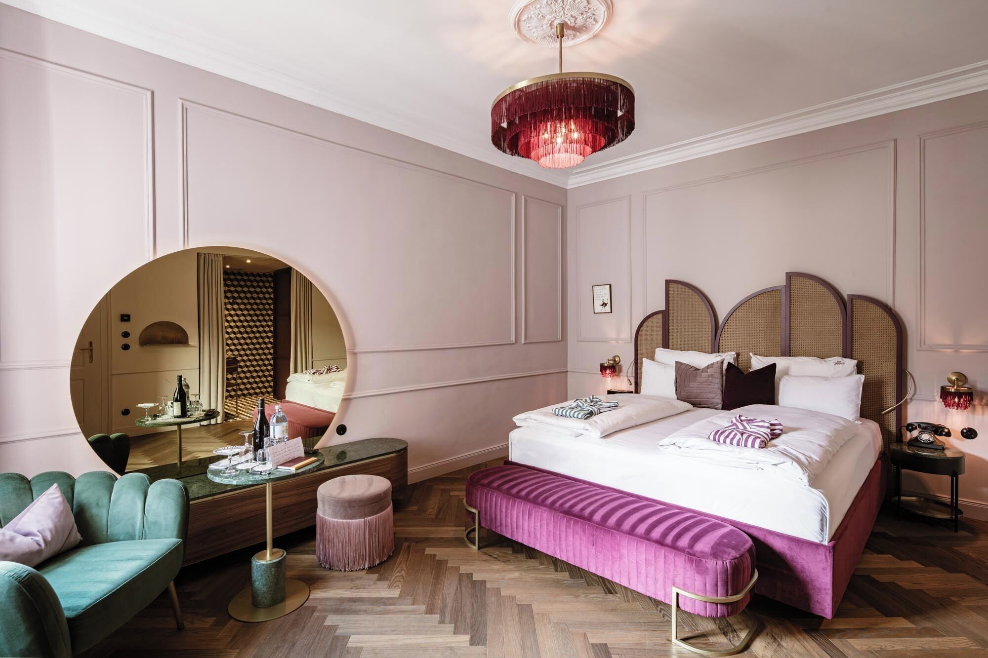 A hotel room with a large bed, a round mirror, a green sofa, and a wooden floor.
