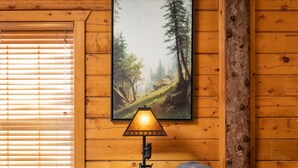 Ein gemütliches Blockhaushaus-Interieur mit einer Holzwand, einem gerahmten Landschaftsbild, einer Tischlampe, einem Ledersofa und einem Holzschrank.