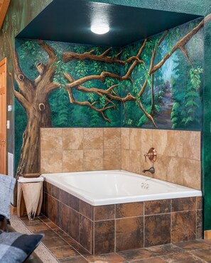 Ein Badezimmer mit einer großen Badewanne, gefliesten Wänden und einer Wandmalerei eines Waldes.