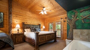 Ein Schlafzimmer einer Holzhütte mit einem Bett, zwei Nachttischen mit Lampen, einem großen Fenster und einem Badezimmer mit einer Badewanne.