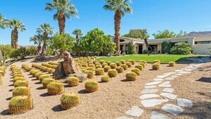 A desert landscape with cacti, palm trees, and a modern building with a patio.