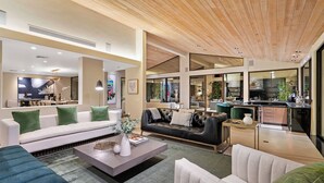 A modern living room with a sofa, armchairs, and a coffee table. There is a kitchen area visible through a glass partition.