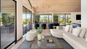 A modern living room with a large sectional sofa, a glass coffee table, and a view of a kitchen and outdoor patio.