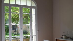 A dining area with a large arched window, a table set for four, and a cabinet with kitchenware. - La Maison d'Antoine (Rivesaltes)