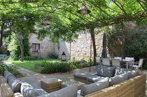 A patio with outdoor furniture, a stone wall, and greenery. - La Maison d'Antoine (Rivesaltes)