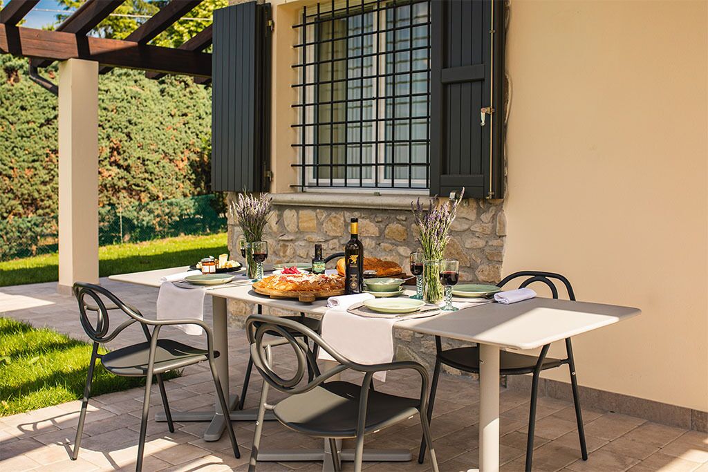An outdoor dining area with a table set for two, surrounded by stone walls and a pergola.